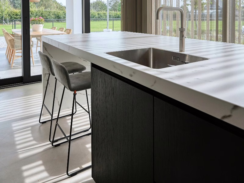 Naadloze gietvloer in een moderne keuken met donker kookeiland en marmerlook werkblad