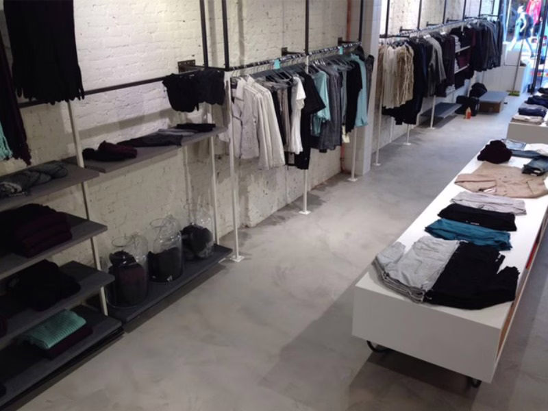 Naadloze betonlook gietvloer in een winkel met kledingrekken en witte bakstenen muren