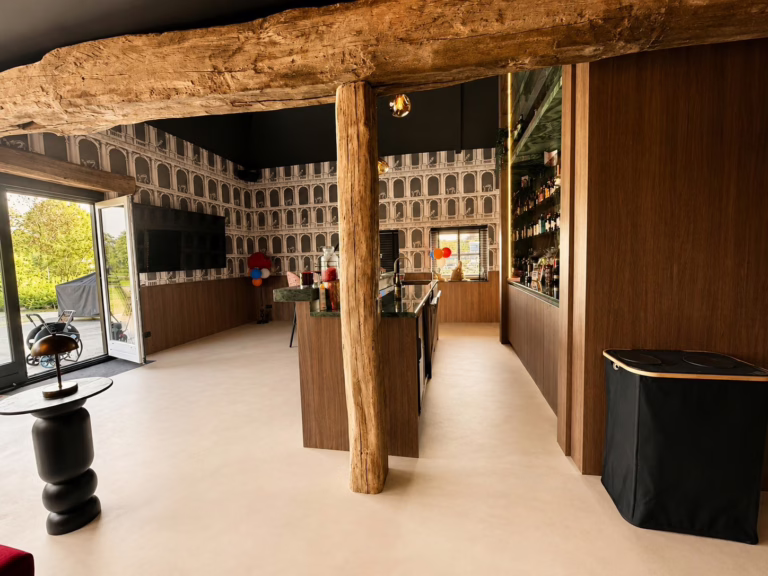 Minimal Sand gietvloer Best — rustieke moderne bar in een gemoderniseerde boerderij met oude houten balken.