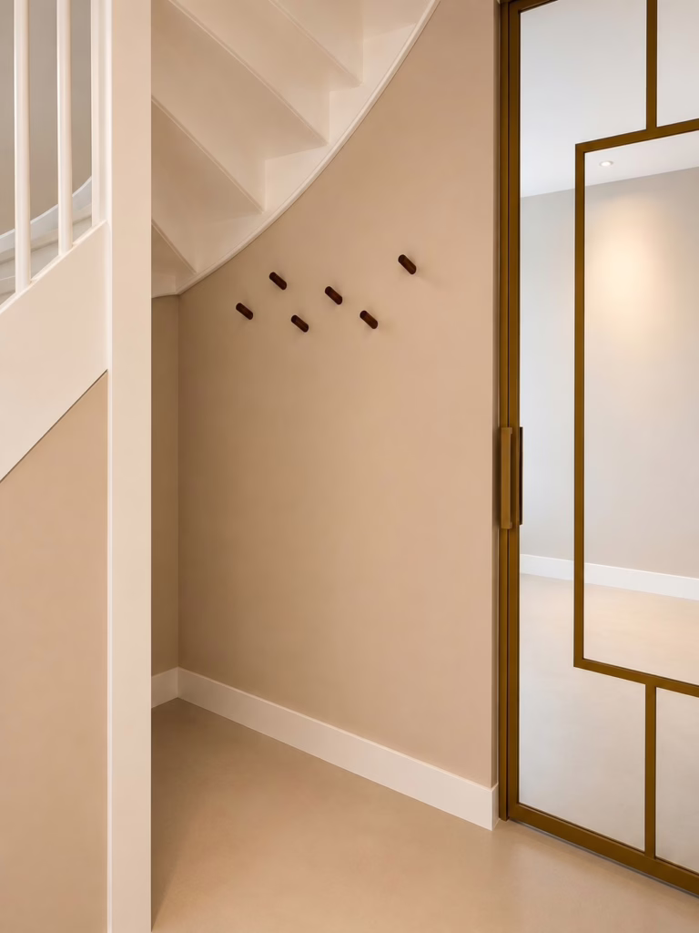 Bio Cement gietvloer Herten — minimalistische hal met witte trap en gouden glazen deur.
