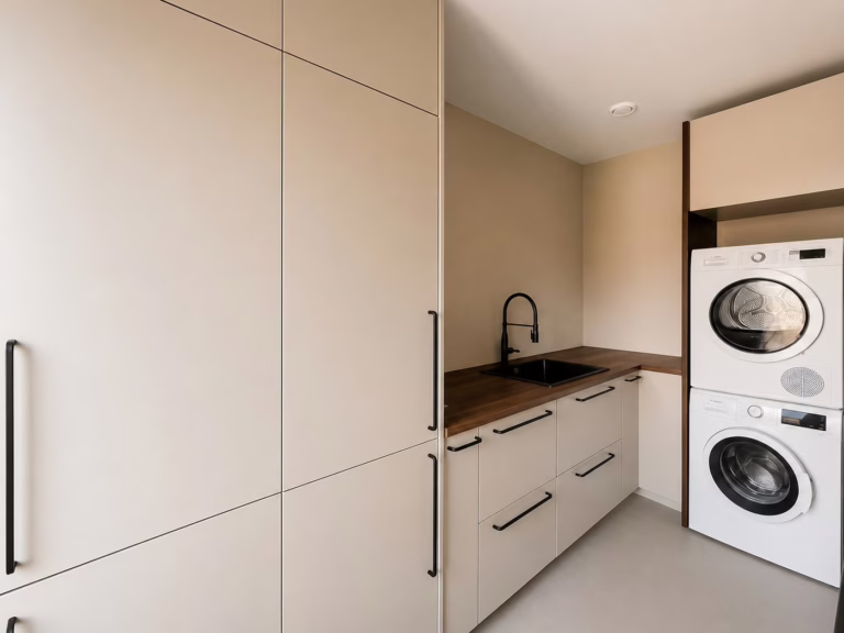 Bio Cement gietvloer Herten — economische wasruimte / bijkeuken met beige maatwerkkasten.