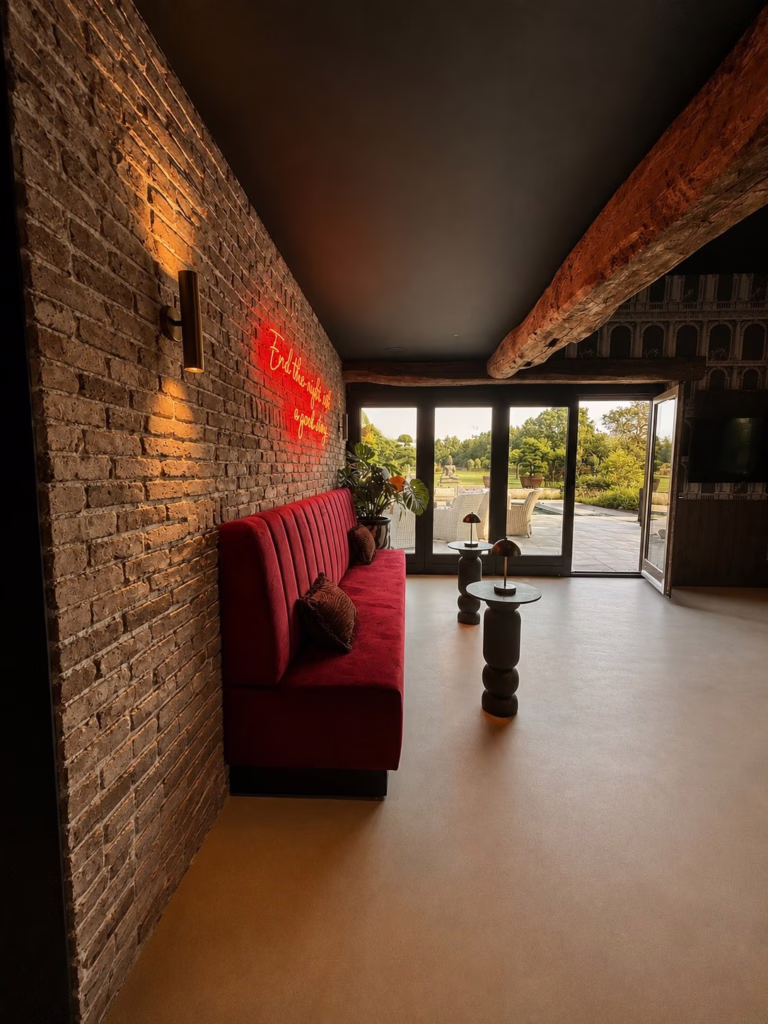 Inspiratie thuisbar op Minimal Sand gietvloer Best — rode bank, gouden lampen en Monstera plant.