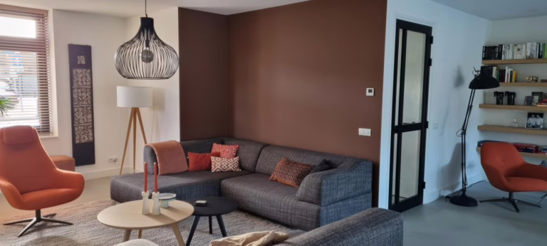 Lavasteen gietvloer Valkenswaard in de woonkamer met bruine accentwand en oranje fauteuils.