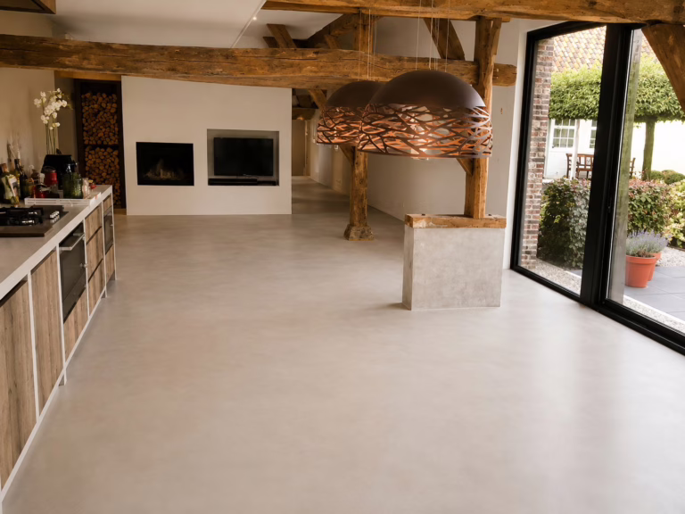 Zithoek met openhaard, houten spanten en pendellampen op een industriele betonnenvloer in Sand Stone, bijgebouw Best