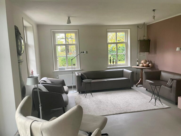 Zitkamer met leren banken en oud-roze accentwand op een gietvloer in de kleur Zandsteen Creme