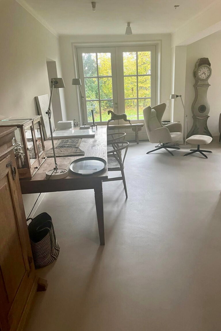 Overzicht van de eetkamer met antieke vitrinekast en Zweedse staande klok op een beige gietvloer