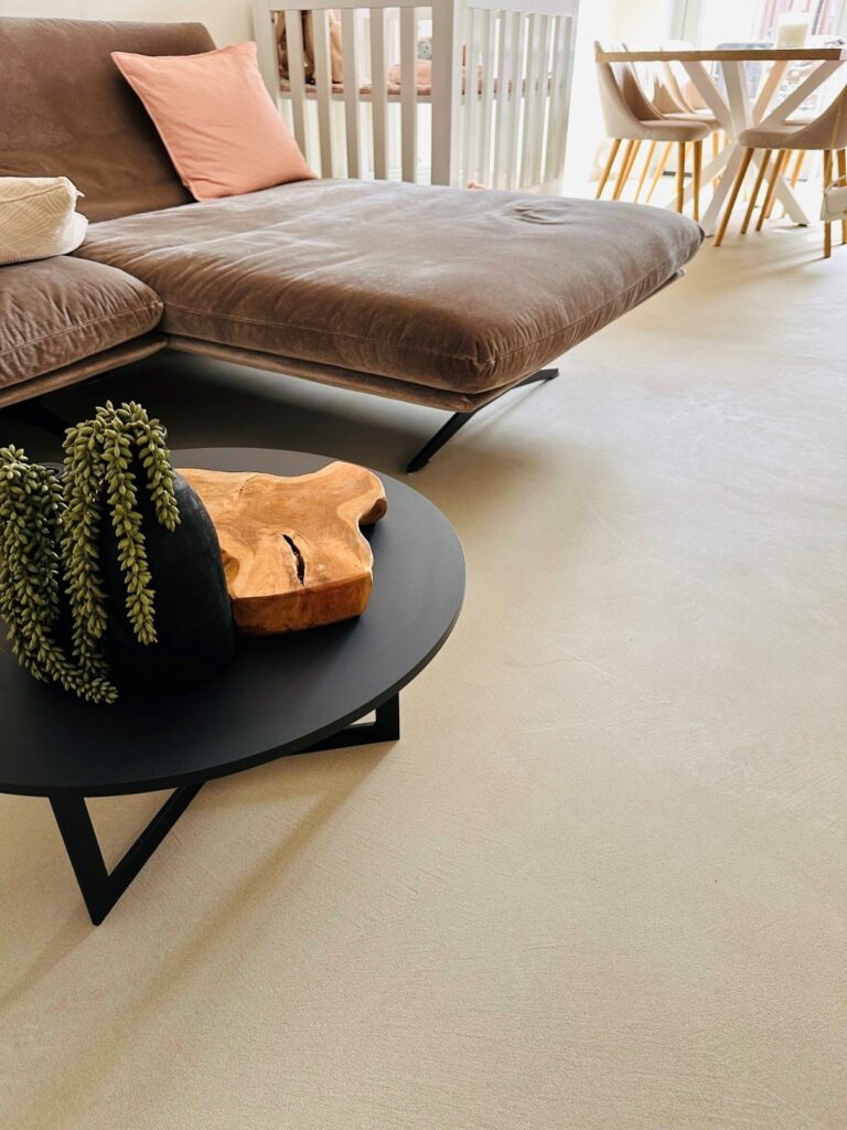 Solido kwartsiet gietvloer in Best in de zandkleur VEIL, met bruine velours bank en zwarte salontafel in een modern Japandi interieur.