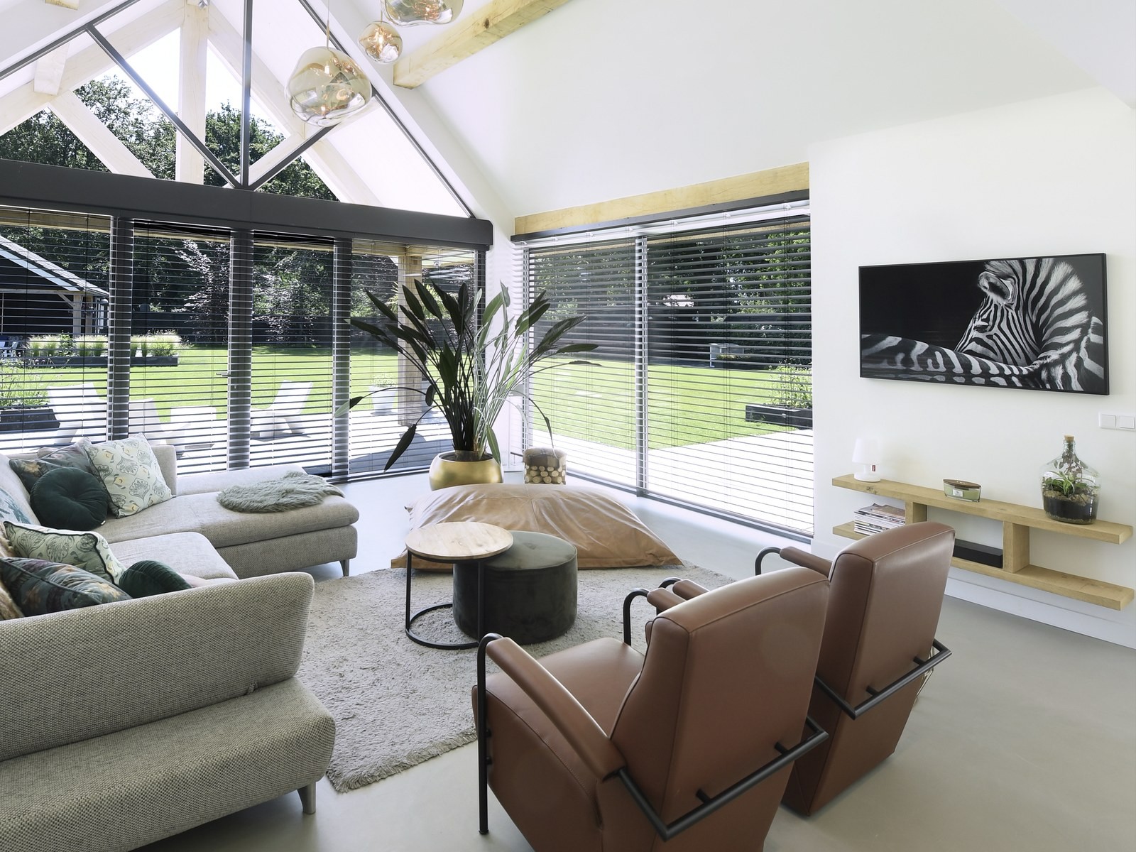 Design Woonbeton in een woonkamer met houten spanten, glazen puntgevel en leren fauteuils 