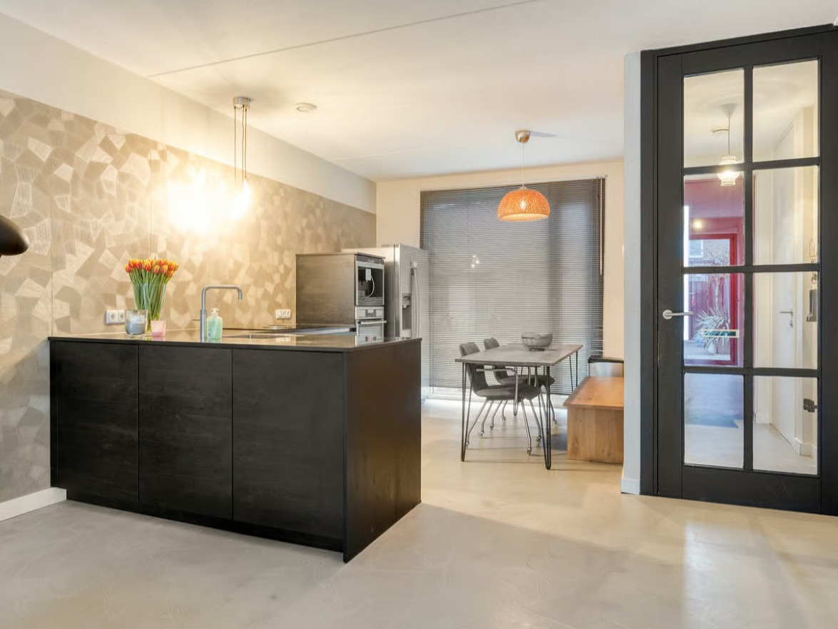 Industriële betonnen vloer Grigio Quarzo keuken Eindhoven ndustriële betonnen vloer in de kleur Grigio Quarzo in een open keuken met zwart keukenblok, eethoek en glazen binnendeur in Eindhoven