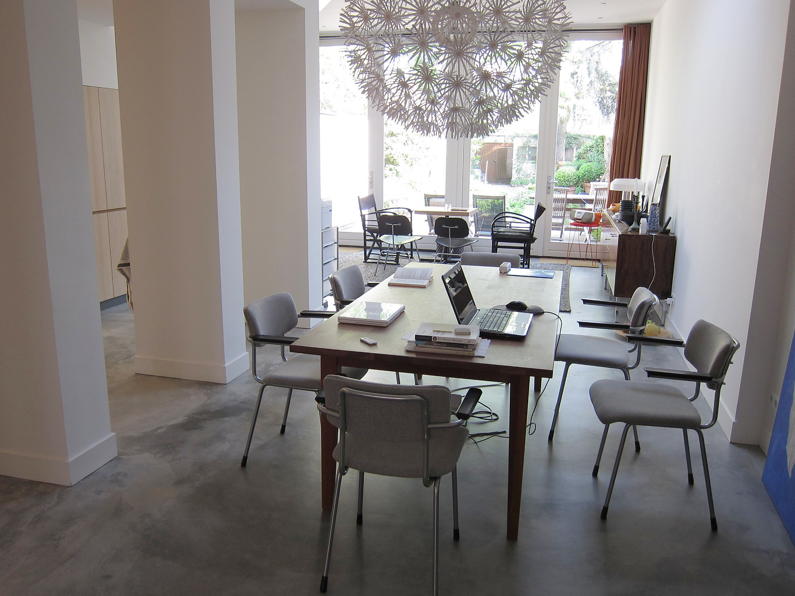 Cementdekvloer met transparante matte coating in een lange woonkamer in Eindhoven, met eettafel, grijze stoelen en tuindeuren